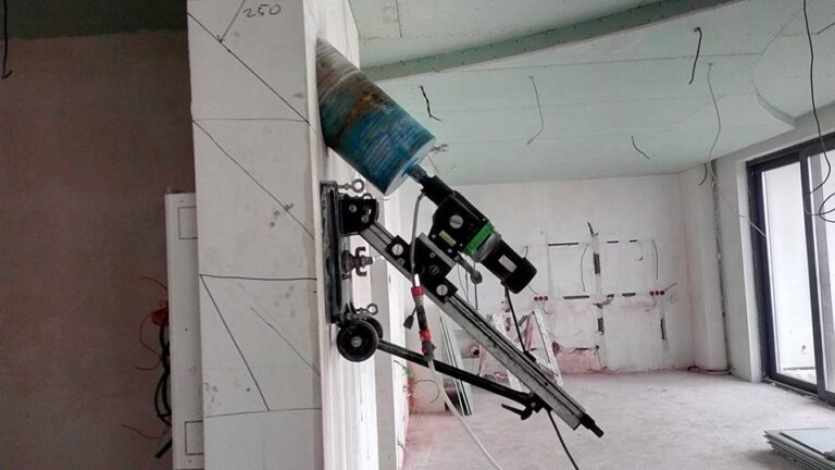 Bohrtechnik in hoher Arbeitsposition. Ein geneigter Bohrständer mit großer Krone ist nahe der Decke im Innenraum montiert.