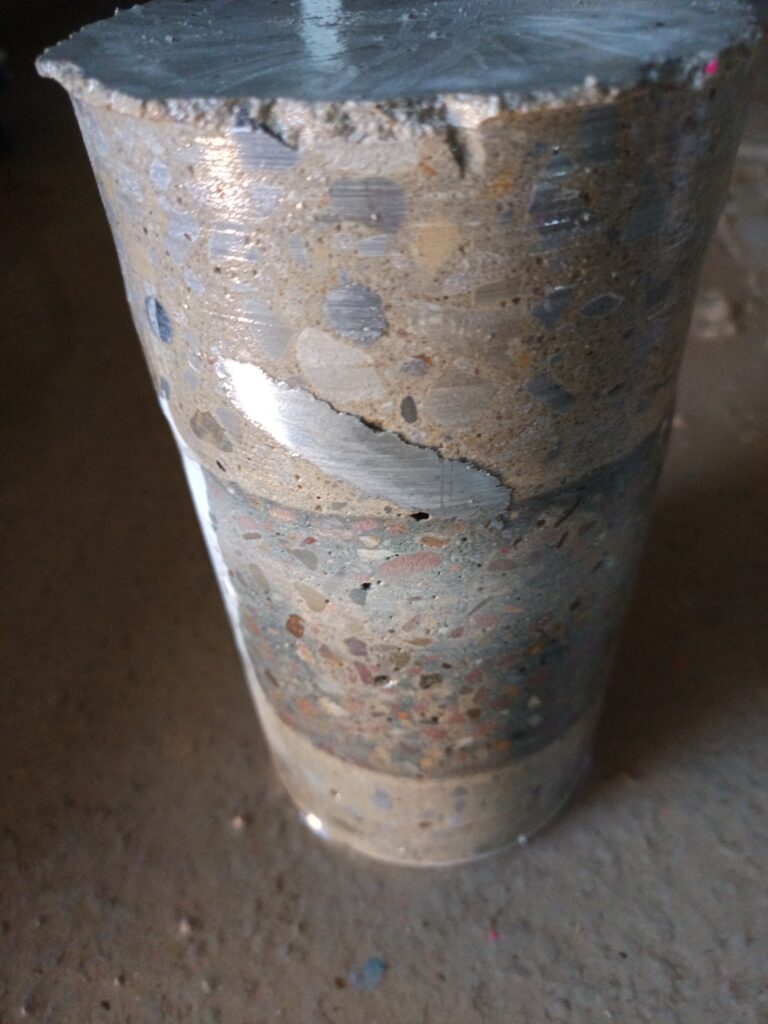 Bohrkern mit sichtbaren Einlagen. Ein entnommener Kern zeigt unterschiedliche Materialbestandteile im Querschnitt.